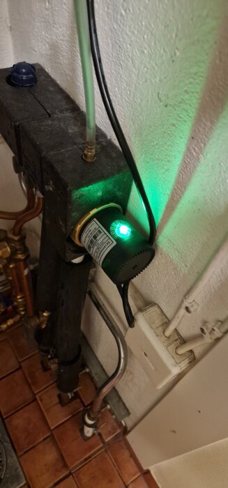 Nyinstallerad drivsida med grön lysdiod kopplad till ledningar, monterad mot vägg ovanför röda klinkerplattor.