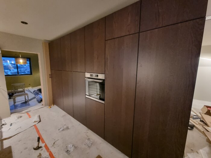 Nyinstallerade köksluckor i mörkt trä med inbyggd ugn, omgivna av byggmaterial under pågående köksrenovering.
