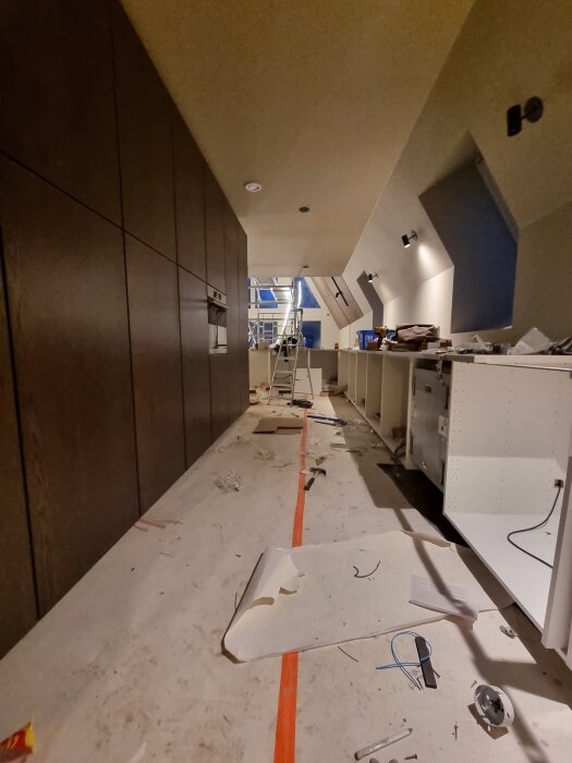 Köksrenovering pågår med golvläggning och montering; verktyg och material är utspridda, en stege ses i bakgrunden.