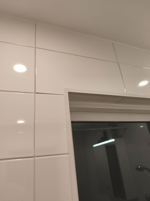 Vitt kakel på badrumsvägg, nyrenoverat med spotlights i taket.