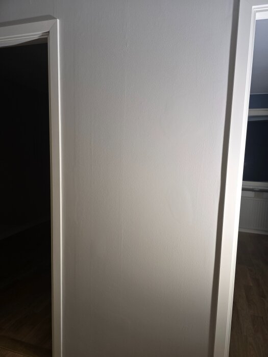 Vägg i lägenhet som nyligen målats om, visar tecken på ojämn slipning och spackling, med synliga skuggor och ojämnheter i ytan.