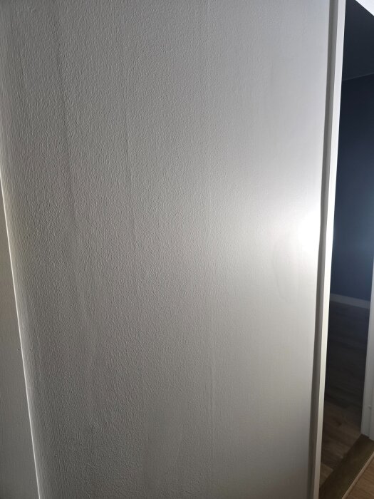 Vitmålad vägg med ojämt resultat efter spackling och slipning, visar brister i hantverk efter borttaget tapet i lägenhetsrenovering.