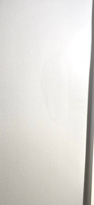 Närbild på en vitmålad vägg med synliga ojämnheter och textur i spacklingen, potentiellt dåligt utfört hantverk av målare.
