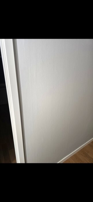 Vitmålad vägg med synliga ojämnheter efter slipning och spackling, visar resultatet av ommålning i en lägenhet.