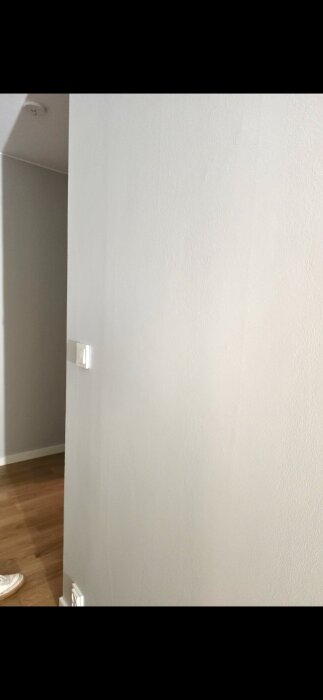 Vägg i lägenhet med synliga ojämnheter och brister i spackling och målning, potentiellt arbete utfört av hantverkare.