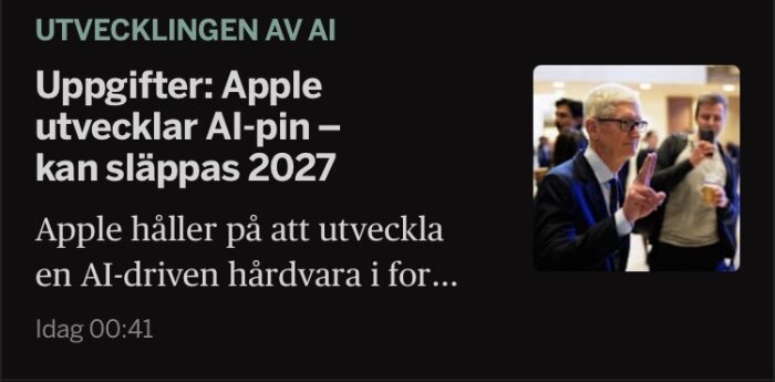 Person i kostym gör handgest, med andra människor i bakgrunden på ett evenemang.
