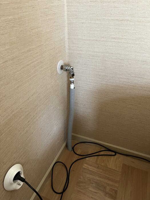 Vattenutkastare monterad i hörnet av ett rum, med grå slang och sladd på trägolv, vilket kan indikera ett problem med installationen.