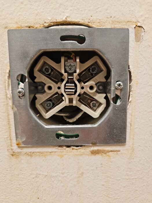 Eluttag utan täckplatta i vägg, visar synliga kopplingar och wires.