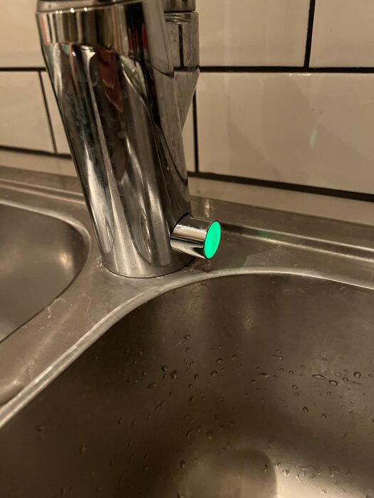 Köksblandare med grön belyst knapp vid sidan av, ovanför en diskho.