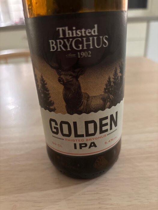 Flaska med Thisted Bryghus Golden IPA, 50 cl, 5,4% vol, på ett träbord.