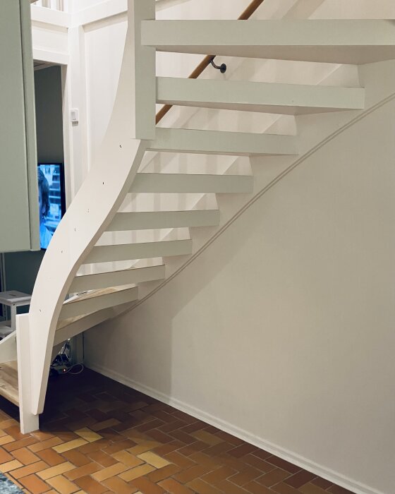 Vitmålad trätrappa med svängda steg, rödbrunt klinkergolv. Enkel modern design med väggmonterad handledare. Elegant och ljus renovering.