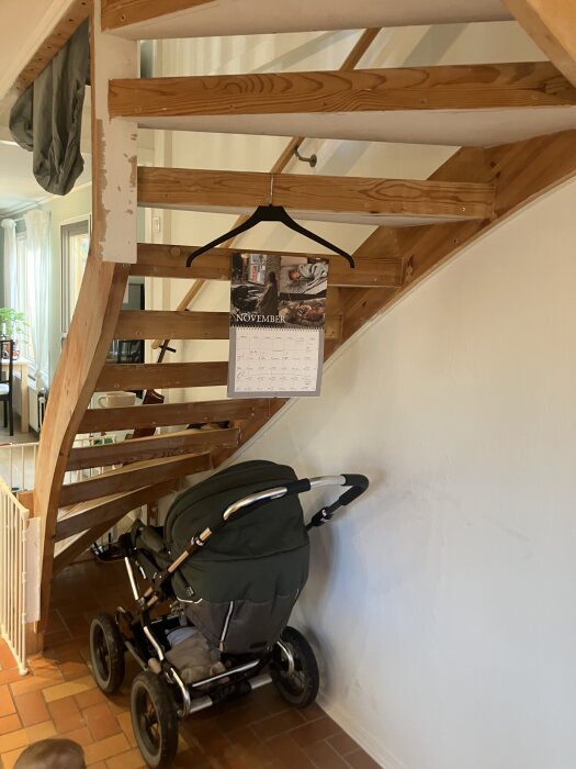 Trätrappa som nyligen renoverats, med en barnvagn under och en kalender hängandes på steget ovanför.