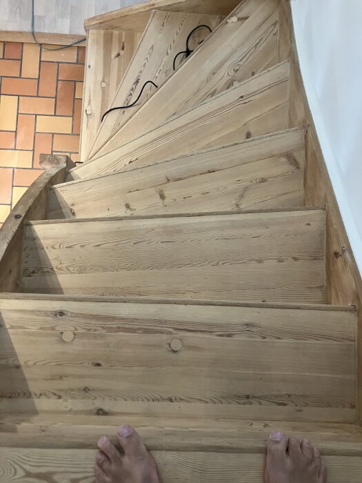 Trappa i trä som nyligen slipats och behandlats, ljus yta med svagt varm ton, ledstång och kabel synliga vid sidan.