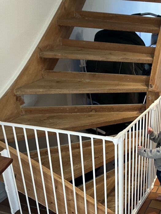 Trätrappa med vit säkerhetsgrind och mörka detaljer, nyslipad och behandlad för ljus ton; del av trapprenovering.