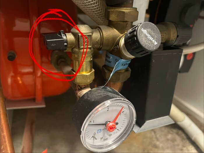 Ventilgrupp med manuella vred och tryckmätare monterade på kopparrör, över ett rött expansionskärl, där en ventil är markerad med en röd cirkel.