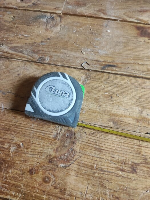 Måttband märkt "Luna" på ett slitet trägolv.