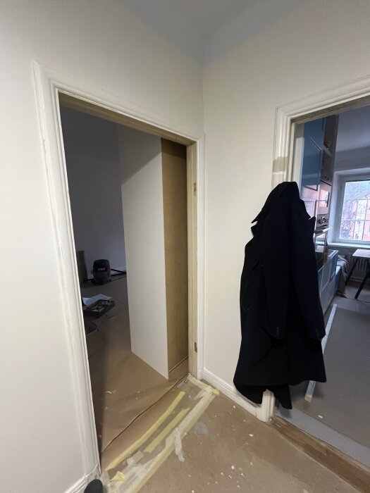 Öppning med borttagen dörr i sovrum. Bevarad karm och dörrfoder syns. Klädhängare med jacka på intilliggande dörr.