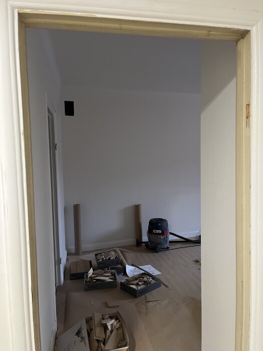Öppen dörröppning utan dörr i ett rum under renovering med verktyg och material på golvet.