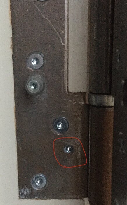 Närbild av dörrgångjärn med justerbar träskruv som djupstopp, markerad med röd ring.