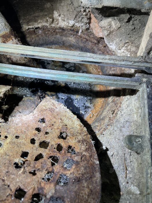 Rostigt avloppsrör med synlig smuts och vattenbubblor under badkaret i ett äldre hus.