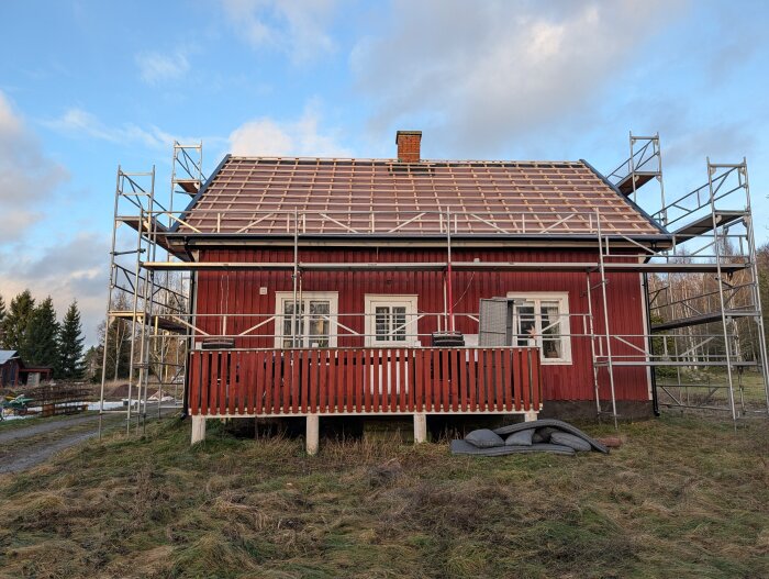 Rött timmerhus under renovering med byggställningar runt, taket visar ny konstruktion med synlig träfiberram.