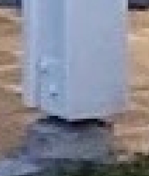 Detalj av en pelare med två brädor påspikade, liknande dimensionerna 90x90 mm, står på en betongyta.