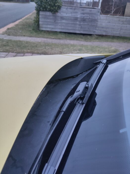 Bilens vindruta med vindrutetorkare och plasten vid botten av rutan som ser ut att sitta lågt.