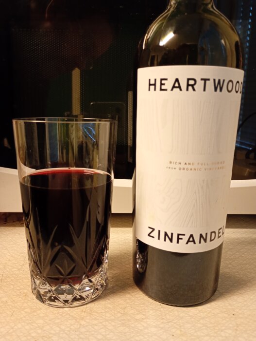 Flaska och glas med Heartwood Zinfandel rödvin på bord.