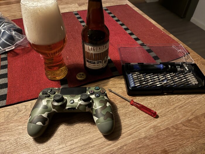 Ölflaska och glas bredvid en verktygssats och spelkontroll på ett bord.
