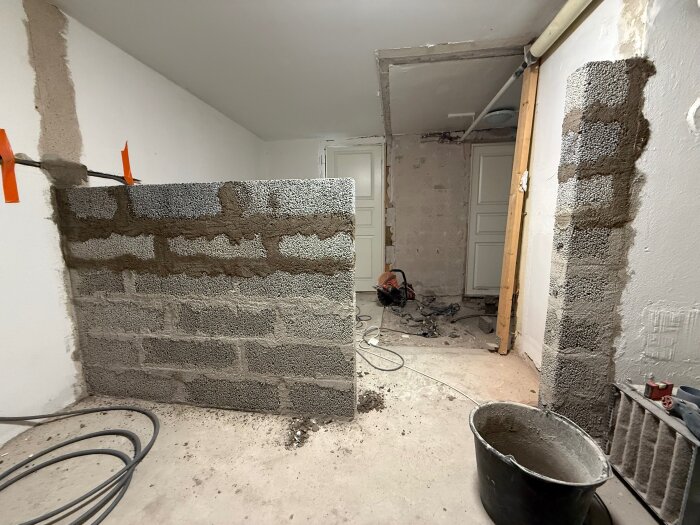 Byggande av innervägg i källare med murblock; en halvfärdig vägg syns tillsammans med byggverktyg och material på golvet.