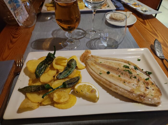 Stekt sjötunga med citron, friterade potatischips och grön paprika serverat på en tallrik på en restaurang, med ett glas öl.