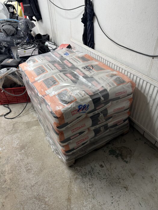 Pall med säckar av Probau flytspackel inslagna i plast, ståendes på ett betonggolv i ett garage med diverse föremål runt omkring.