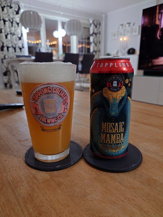 Ölglas och burk med Toppling Goliath Mosaic Mamba Double India Pale Ale på ett bord i ett vardagsrum.