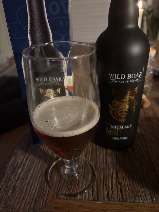 Flaska och glas med Wild Boar årgångsöl, golden ale med mörk rom, 10% alkohol, på ett bord med text på etiketten.