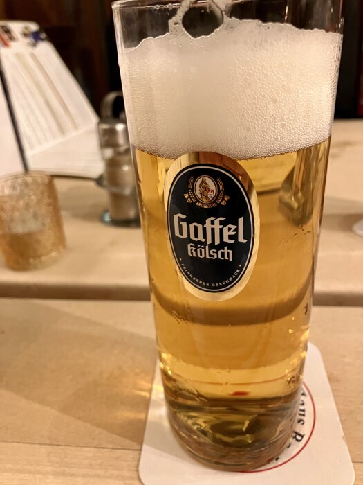 Ett glas öl med skumkrona på ett bord, märkt med etiketten "Gaffel Kölsch".