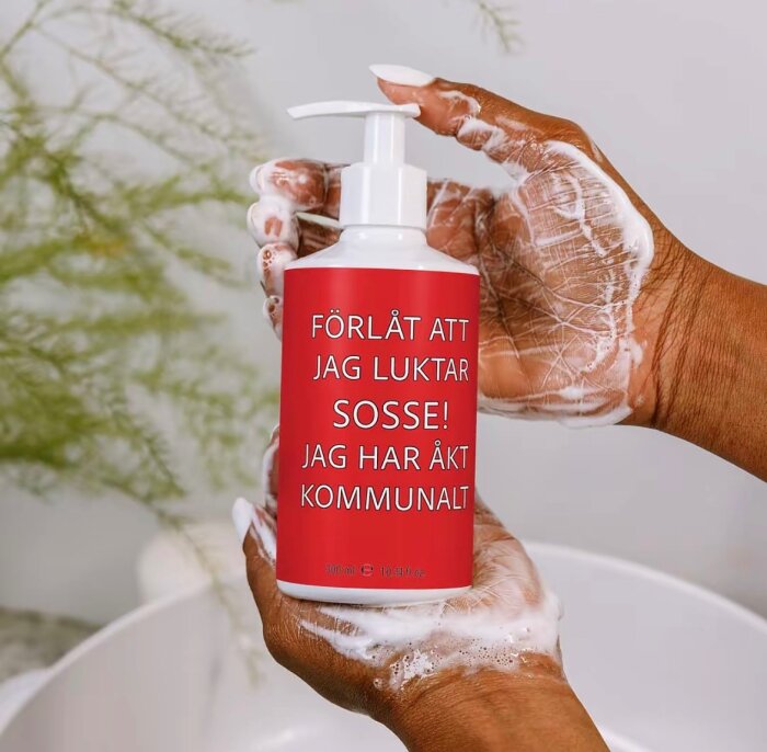 Två händer med lödder håller en tvålflaska med röd etikett och texten: "FÖRLÅT ATT JAG LUKTAR SOSSE! JAG HAR ÅKT KOMMUNALT".