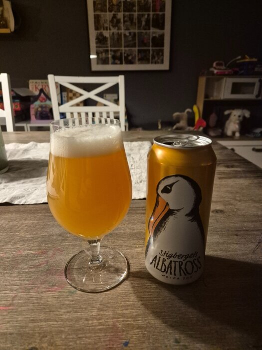 Ett glas gyllene öl med skum och en ölburk med logotyp på ett bord.