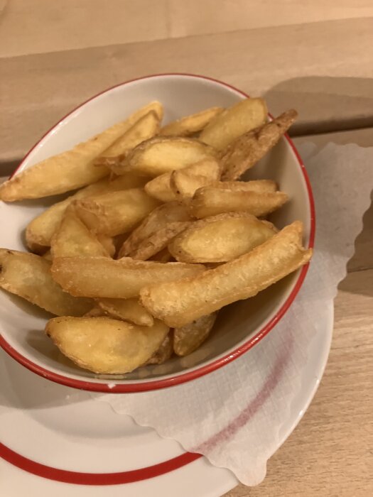 En skål med gyllene, friterade potatisklyftor på ett bord.