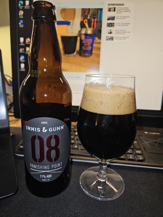 Ölflaska och glas med mörk öl framför en dator, öl av märket Innis & Gunn.