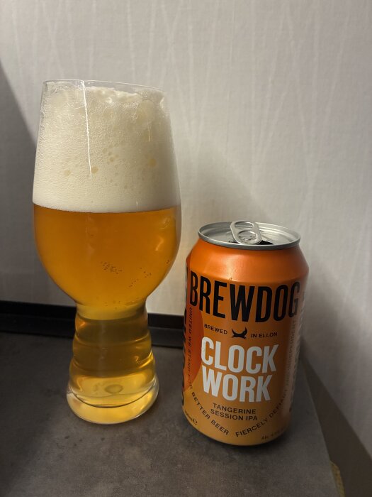 Ett glas öl med skumkrona bredvid en burk Brewdog Clockwork Tangerine Session IPA.