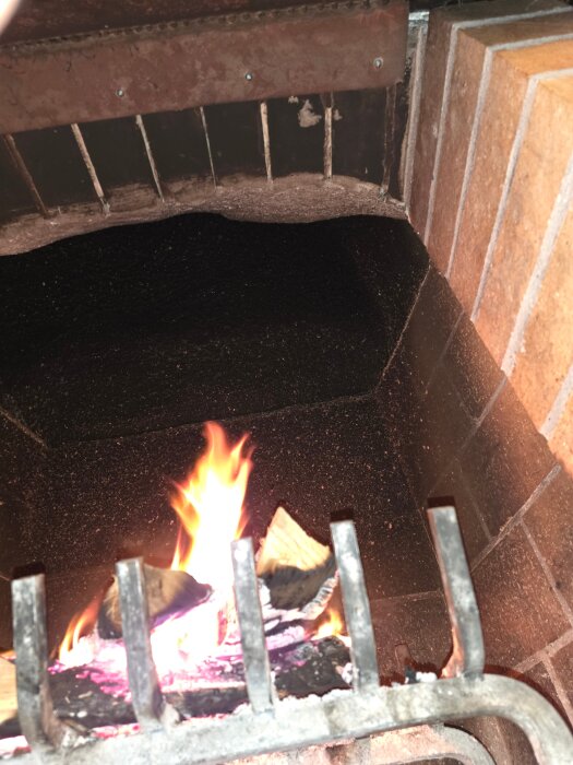 Öppen spis med brasa, träbitar brinner, inplacerad i en tegelklädd eldstad, set för experiment i värmeåtervinning.
