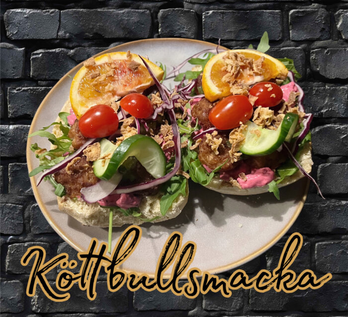 KöttbullsmörgÄs med gurka, körsbÀrstomater, rödlök, apelsinskiva och sallad pÄ ett fat, mot en svart bakgrund.