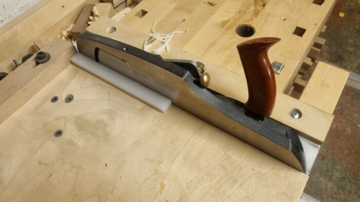 Handhyvlad miter bar av POM-plast på ett arbetsbord, med trähandtag och justeringsskruvar. Verktyget används för precisionshyvling.