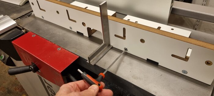 Hand håller en insexnyckel och justerar en aluminiumprofil med miter bars på en arbetsbänk inom ett byggprojekt.