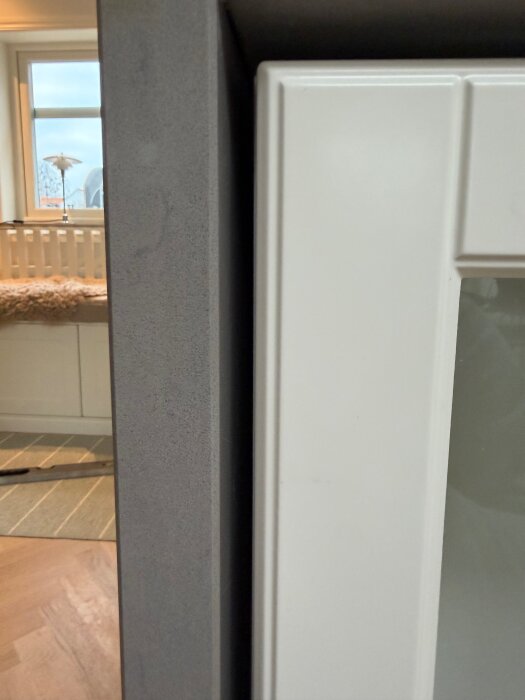 Mellanrum mellan vit bänkskåpskant och grå stenskiva på en köksö, som behöver täckas; mäter cirka 7 mm åt sidorna och 15 mm uppåt.