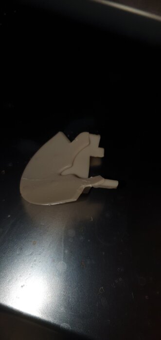 Vit plastdetalj från en diskmaskin som ligger på en mörk yta.