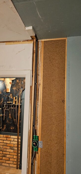 Vägg och tak under renovering med borttagna garderober, synliga gipsplattor och kablage, samt en del av en murad vägg med dekorativa föremål.