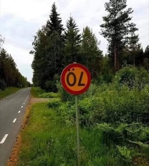 Vägskylt bredvid en landsväg vid skogskant, där skylten är modifierad att visa ordet "ÖL" i stället för standardtext.