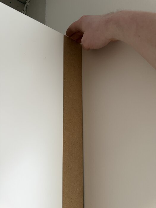 En hand greppar kanten på en dörr, med en trälist placerad en centimeter in.