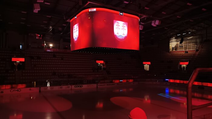 En ishockeyarena med ljusspel på isen och ett stort rött scorebord i mitten som visar en logotyp med texten "Timrå IK".